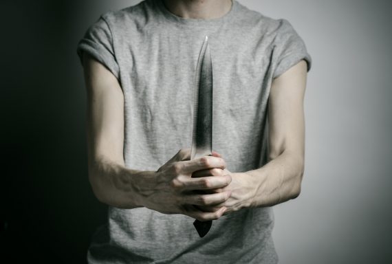 Murder and Halloween theme: a man holding a knife on a gray background