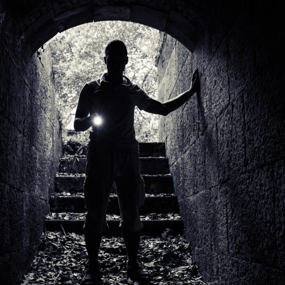 Young man with a flashlight enters the stone tunnel